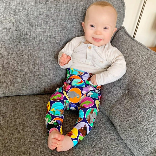 Colourful harem pants on an older baby, resting in the corner of the sofa. The baby has down's syndrome and is smiling at the camera.