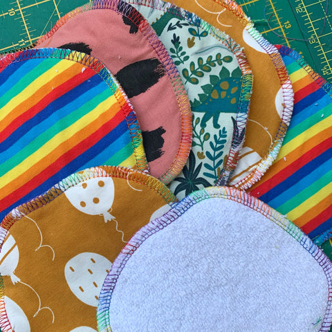 A piles of wipes in mixed prints, one showing the white terry towelling backing. Each has rainbow stitching.